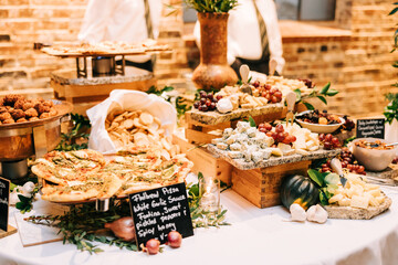 Appetizer buffet with cheese, fruit, and canapés on a white table at a wedding reception. 