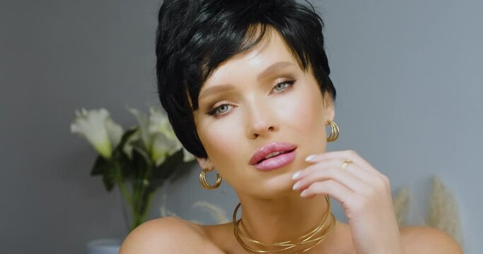 A luxurious young Caucasian brunette with a short haircut looks seductively at the camera and smiles slyly. He enjoys his beauty and tries to seduce you. Slow motion 4k footage.