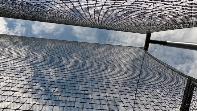 Sports Nets Against a Cloudy Blue Sky. Looking up a sports netting used to enclose a batting cage. Stationary view with wind creating motion in the netting. Black net set against a cloudy blue sky. 