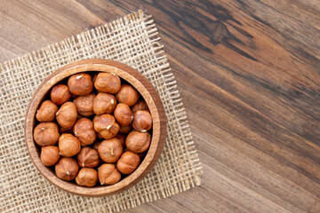 Overhead view of a bowl full of hazelnut kernels on a wooden surface