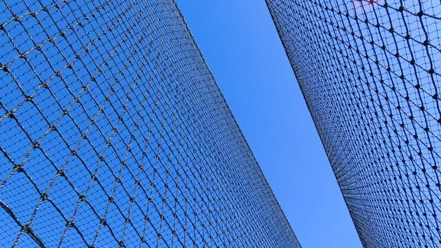 Sports Nets Against a Clear Blue Sky. Looking up a sports netting used to enclose a batting cage. Stationary angled view with wind creating motion in the netting.