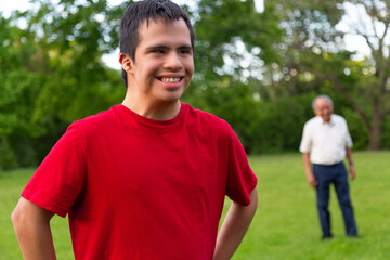 A young man in a red shirt is smiling and standing in a grassy field