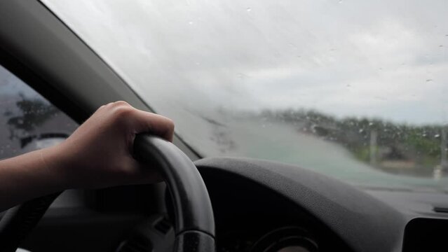 close-up of a male driver's hands on the steering wheel of a car vr while traveling in rainy weather. The windshield wipers wipe the rain off the windshield.
