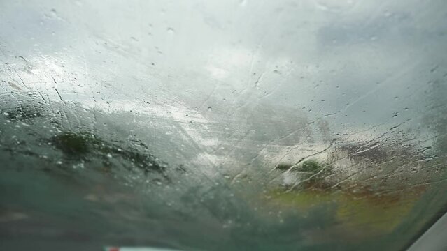 Close-up POV from inside a car onto raindrops on the windshield. Traveling on a wet road on a rainy day. First person view car passenger. Wipers wipe the foggy windshield from raindrops