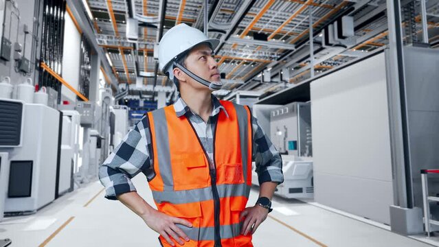 Asian Male Engineer Wearing Safety Helmet Looking Around While Standing With Arms Akimbo At Factory Digitalization