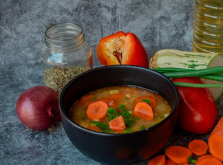 La imagen muestra un tazón de sopa con trozos visibles de verduras, como zanahorias y posiblemente...