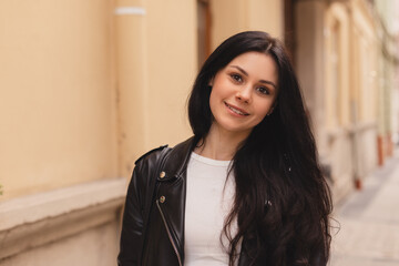 Outdoor portrait of beautiful brunette woman standing on the street, walking outdoors. Girl wear black leather jacket. Tourist woman walking outside.