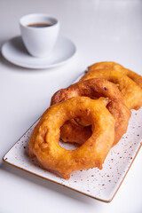 Traditional Peruvian dessert called Picarones, served on a white tray next to a cup of coffee.