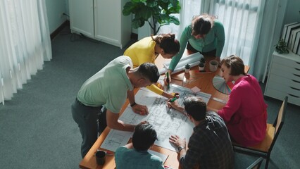 Top view of civil engineer team writing at blueprint at meeting table with color palettes. Group of...
