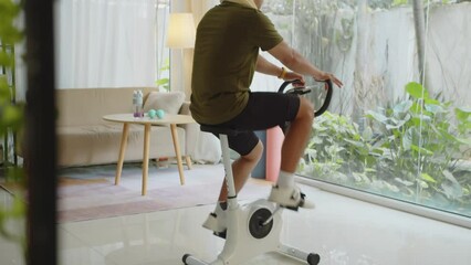 Tilt up shot of sporty man wearing VR headset when training on fitness bike at home