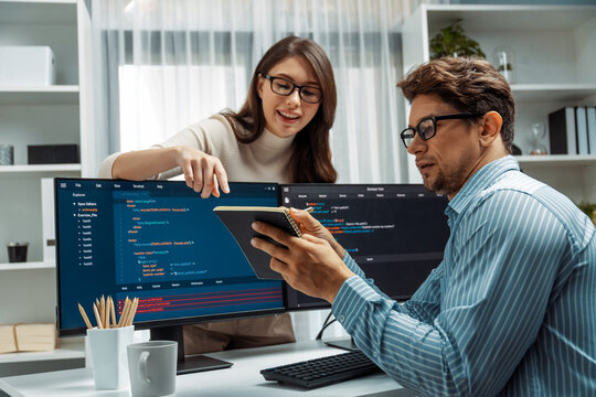 Woman colleague standing opposite to man programmer working on desk to discuss coding website software system project on two pc screen, comparing with typing full stack data prompt design. Postulate.