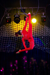 Professional aerial hoop woman gymnast circus performance at blue arena with dark background backlit with colored concert lights, performing gymnastic element © Michael Rekochinsky