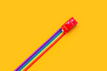 Blue toy car, rainbow ribbon flag trail road, yellow background. June gay parade, proud month, coming out day, human rights and tolerance concept. Minimal pop art composition. Flat lay, top view