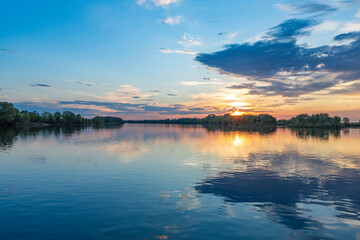 The sun is casting a warm golden glow as it sets over the calm waters of a lake, creating a serene and magical atmosphere.