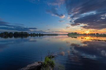 Fototapeta premium A scenic view of a river at sunset, with a peaceful and calming atmosphere. The water reflects the golden hues of the sky, creating a beautiful and serene image.