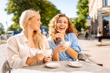 Friendship concept. Two girlfriends women eating breakfast in city cafe together while gossiping...