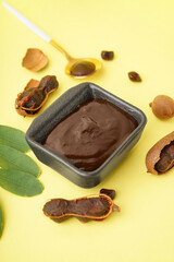 Bowl with tasty tamarind jam with fruits on yellow background