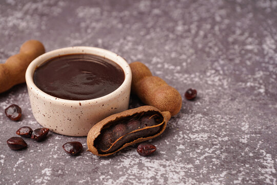 Bowl with tasty tamarind jam and fruits on grey background