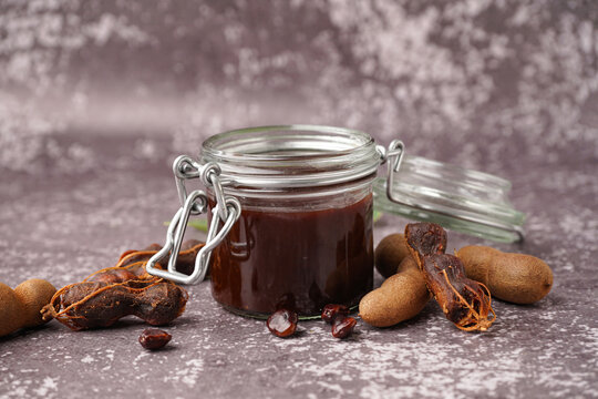 Jar with tasty tamarind jam and fruits on grey background
