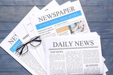 Newspapers with glasses on blue wooden background