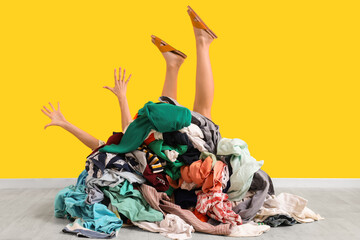 Young woman buried under pile of dirty laundry on yellow background