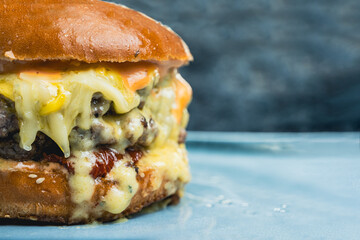 An extreme closeup of a cheeseburger on a white plate against a grey background. Melted cheese drips down the sides of the burger, creating a visually appealing and appetizing image with copy space.