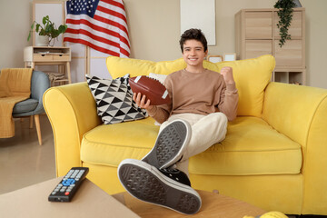 Teenage boy with rugby ball watching football match at home