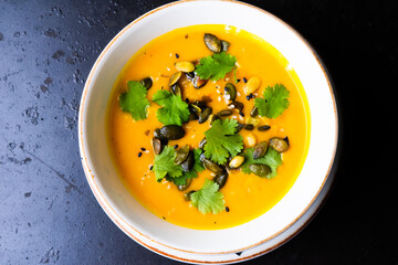 Pumpkin cream soup with parsley on gray stone and wooden background. Top view, copy space