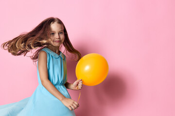 Little girl in blue dress holding orange balloon against vibrant pink background