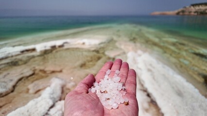 Close-up view of a hand presenting natural salt crystals against the picturesque backdrop of the...
