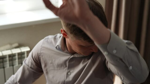 Closeup tracking shot of young man in shirt with disgust checking sweaty armpits while working on computer sitting at desk. Gland problems. Hyperhidrosis, increased sweating, anhidrosis, slow motion.