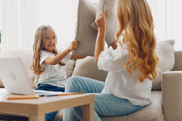 Mother and daughter bonding time on cozy couch with pillows, enjoying laptop activities together in...