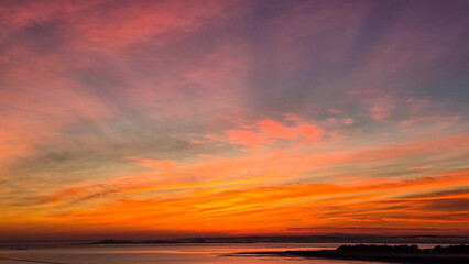 A vibrant sunrise with hues of pink, orange, and yellow unfurls across a blue sky above a reflective ocean.
