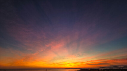 A vibrant sunrise with hues of pink, orange, and yellow unfurls across a blue sky above a reflective ocean.