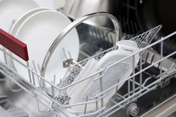 Close up of a full dishwasher with clean plates, lids, glassware in the kitchen