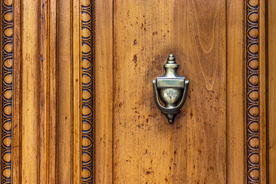 Detalle de puerta antigua de madera con aldaba y decoraciones talladas, de color ocre.