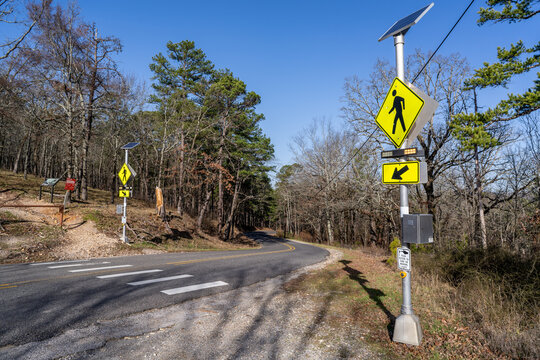 A pedestrian crossing with diamond shape warning sign and solar power button operated lights on a pole in a forested, rural mountain environment, Sunset Trail, Hot Springs National Park, Arkansas