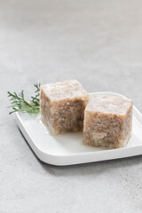 Aspic. Jellied meat in the shape of a cube. On a plate. Light gray background	