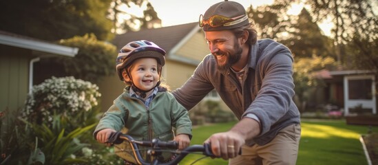 portrait of an active father helping teach his young son to learn to ride a bicycle while wearing a safety helmet in the yard of their family home