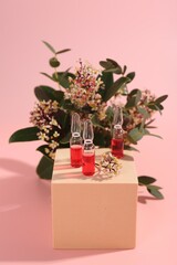 Stylish presentation of skincare ampoules and flowers on pink background