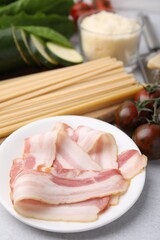 Raw pasta, bacon and fresh ingredients on light grey table