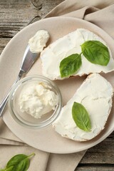 Delicious sandwiches with cream cheese and basil leaves on wooden table, top view