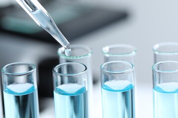 Dripping liquid from pipette into test tube on blurred background, closeup