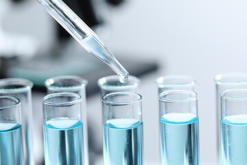 Dripping liquid from pipette into test tube on blurred background, closeup