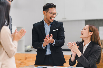 Group of business professionals in modern office clap and smile, celebrating a successful meeting or achievement.