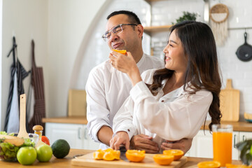 Young asian family couple having fun cooking and preparing cook vegan food healthy eat with fresh vegetable salad on counter in kitchen at home.Happy couple looking to preparing food