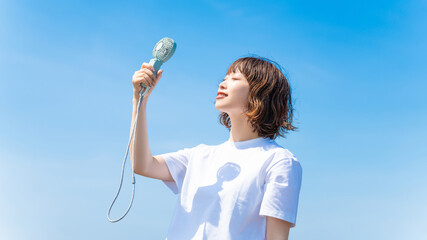 ハンディファンで涼む白いTシャツ姿の女性・熱中症対策