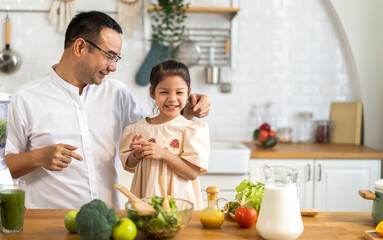 Joyful moment of father and daughter cooking together in modern kitchen, father guiding daughter prepares fresh salad with various vegetables and ingredients, healthy eating and home cooking at home