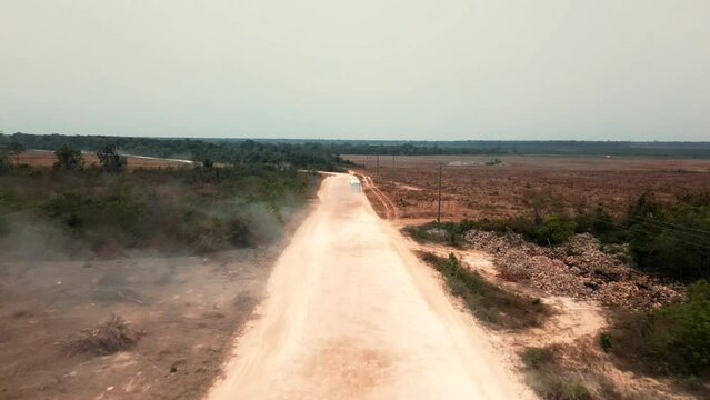 Seguimiento de autobus sobre camino de tierra sembradio seco y bosque Distrito Corozal Belice centroamerica camino de terraceria en paisaje desertico