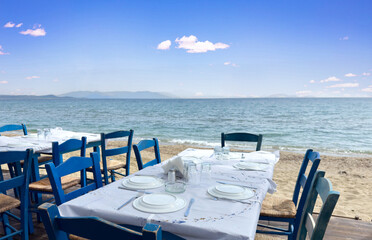 Open-air traditional seaside tavern restaurant in Greece. Empty blue chair laid table with dish.